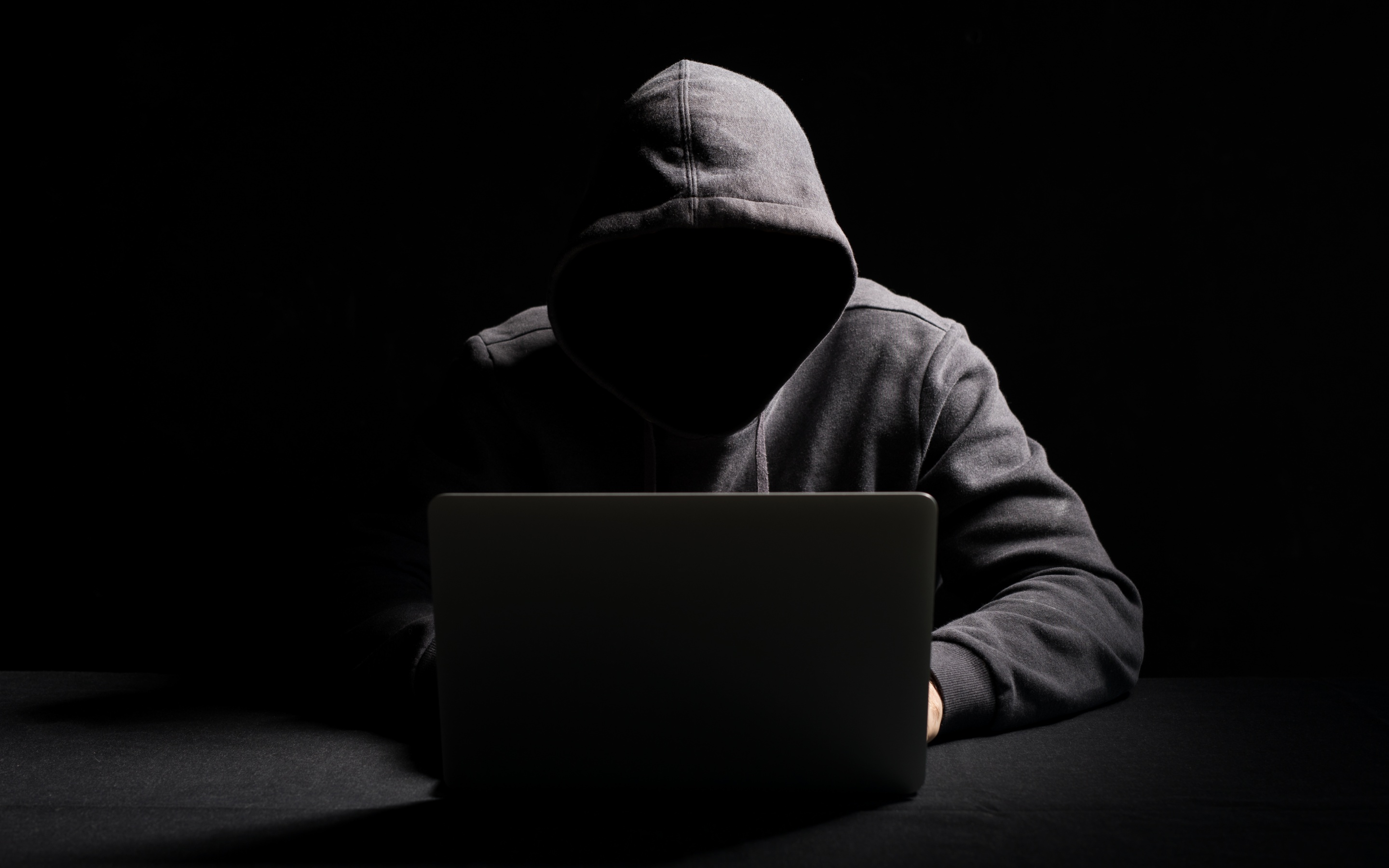 Hooded cybersecurity professional working on a laptop